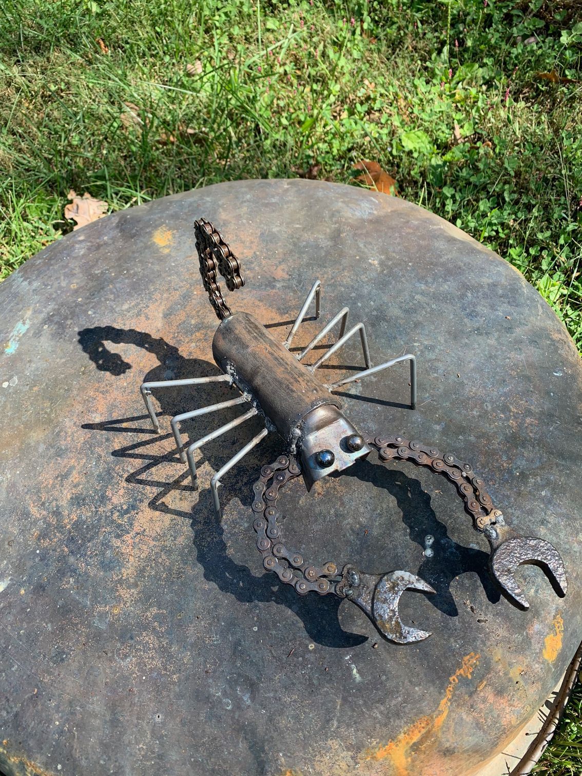 A metal scorpion is sitting on top of a metal barrel.