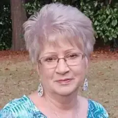 A woman wearing glasses and a blue shirt is standing in a field.