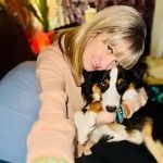 A woman is sitting on a couch holding a dog.