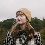 A woman wearing a hat and a plaid shirt is standing in a field.