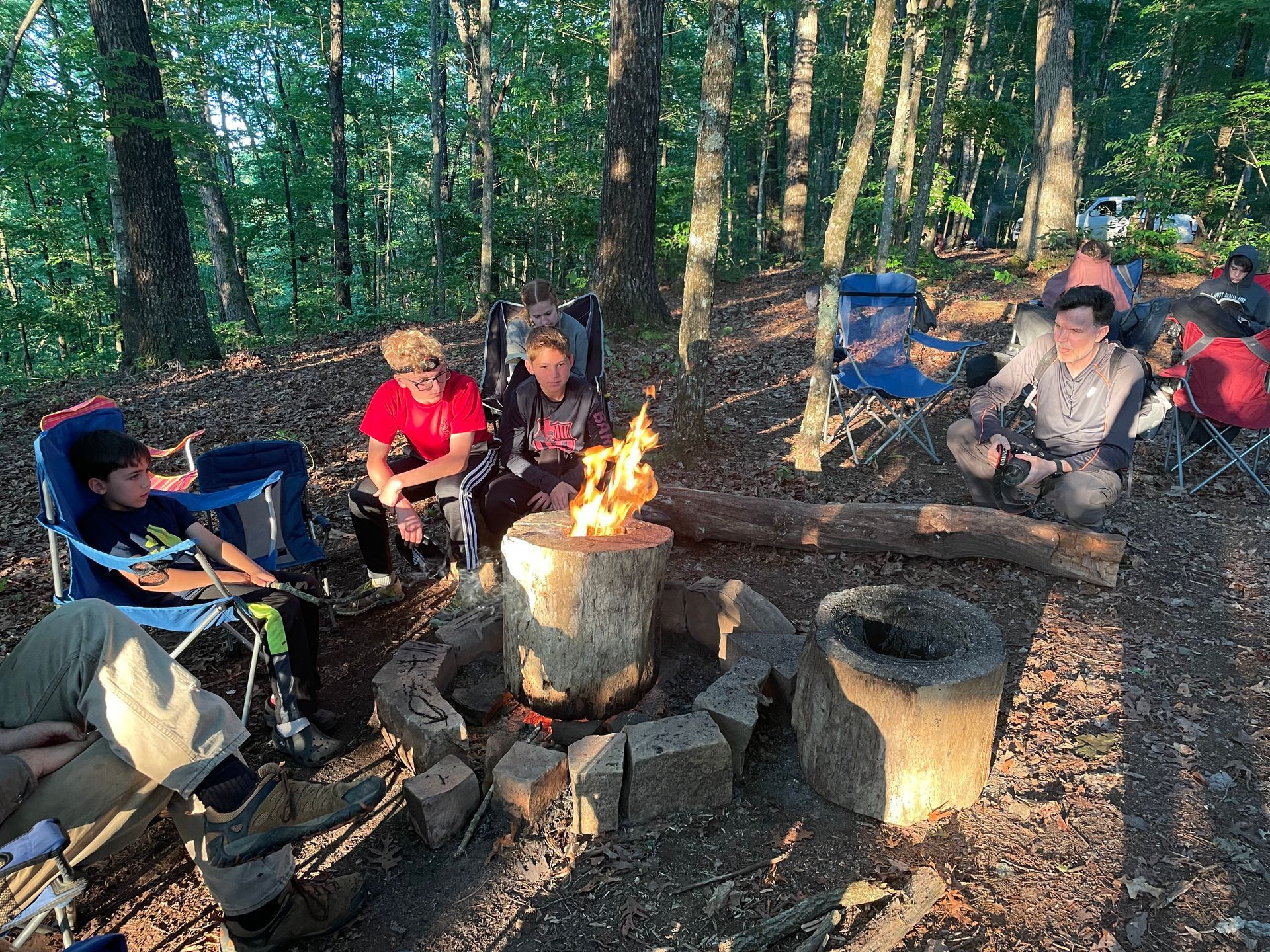 A group of people are sitting around a fire pit in the woods.