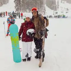 A man and a woman are standing in the snow holding snowboards.