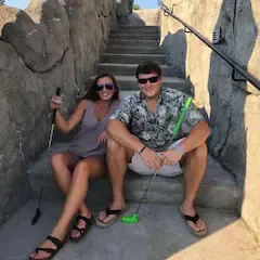 A man and a woman are sitting on a set of stairs holding golf clubs.