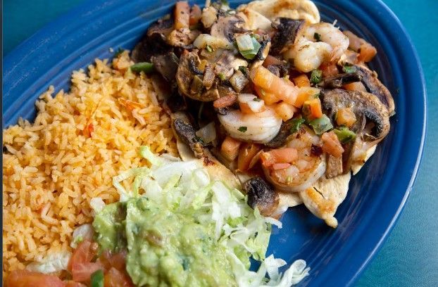 A blue plate topped with rice , guacamole , and shrimp.