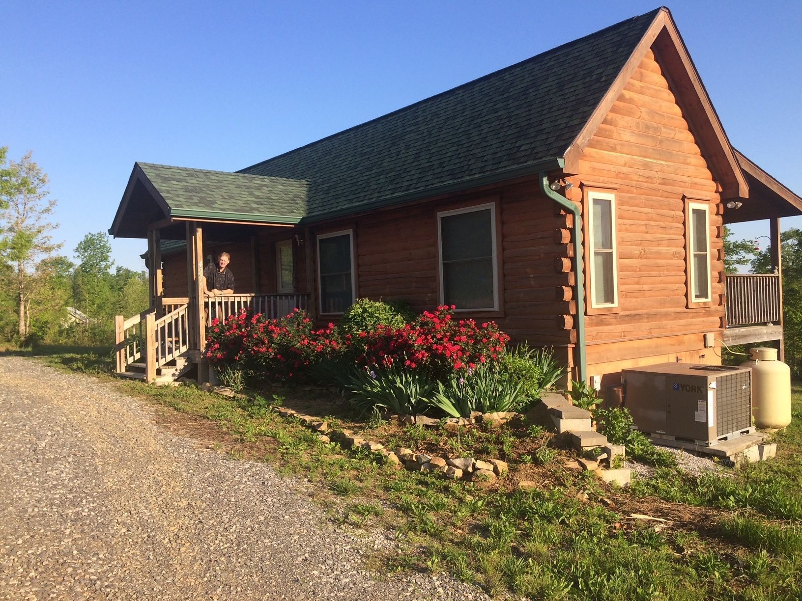 A man is standing on the porch of a small log cabin.