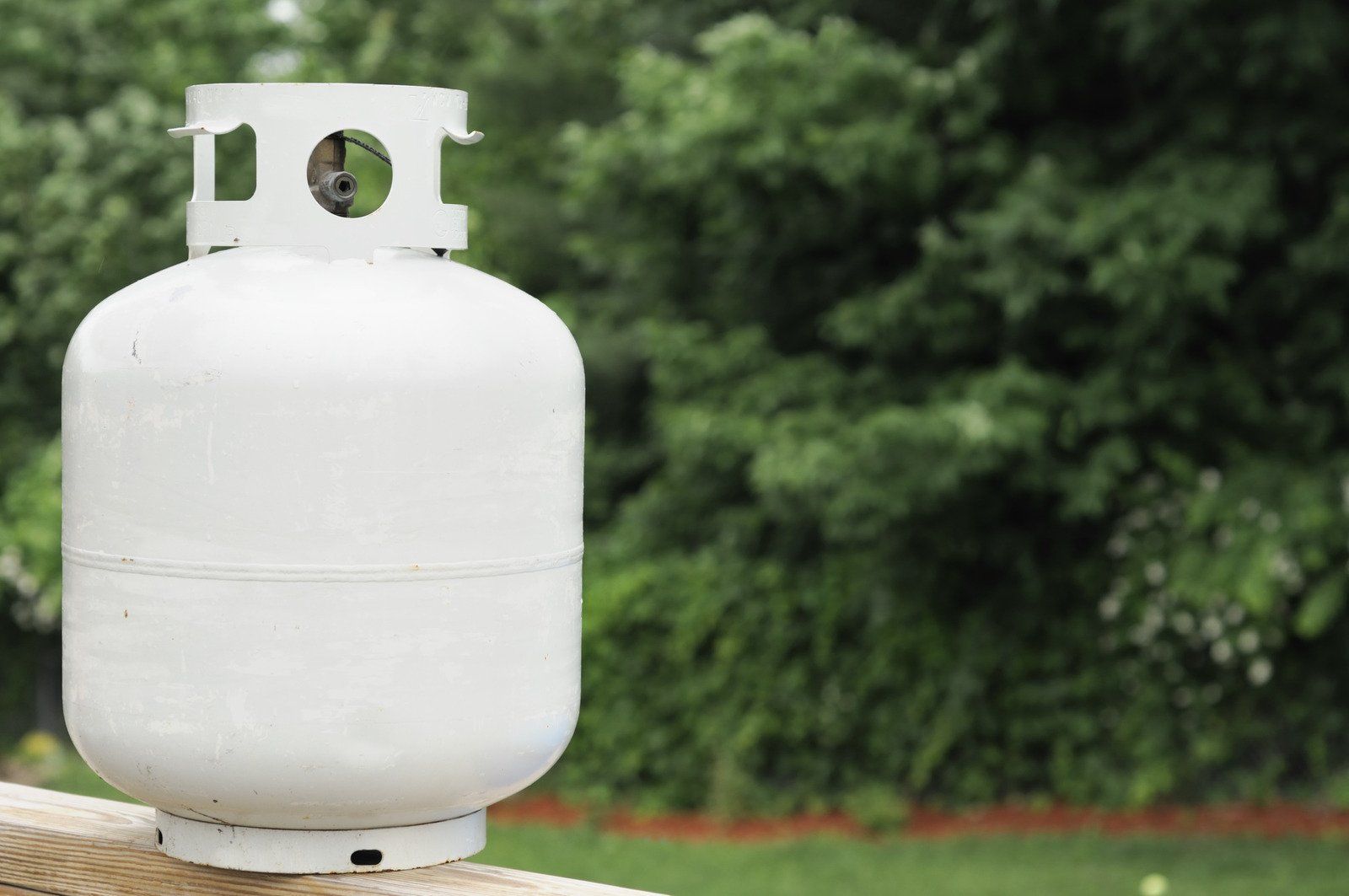 A white propane tank is sitting on top of a wooden railing.