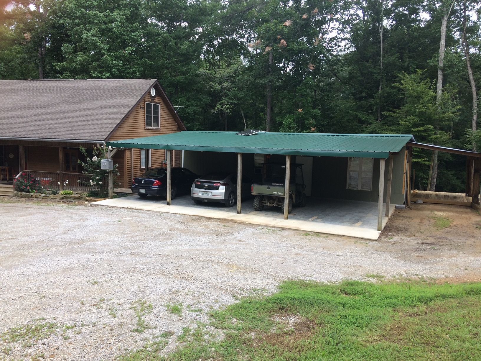 A carport with cars parked underneath it in front of a log cabin.