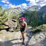 A woman is standing on a rocky trail in the mountains.