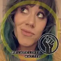 A woman with green hair and a fist in a circle is smiling.