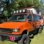 An orange van with lights on the roof is parked in the grass in front of a house.