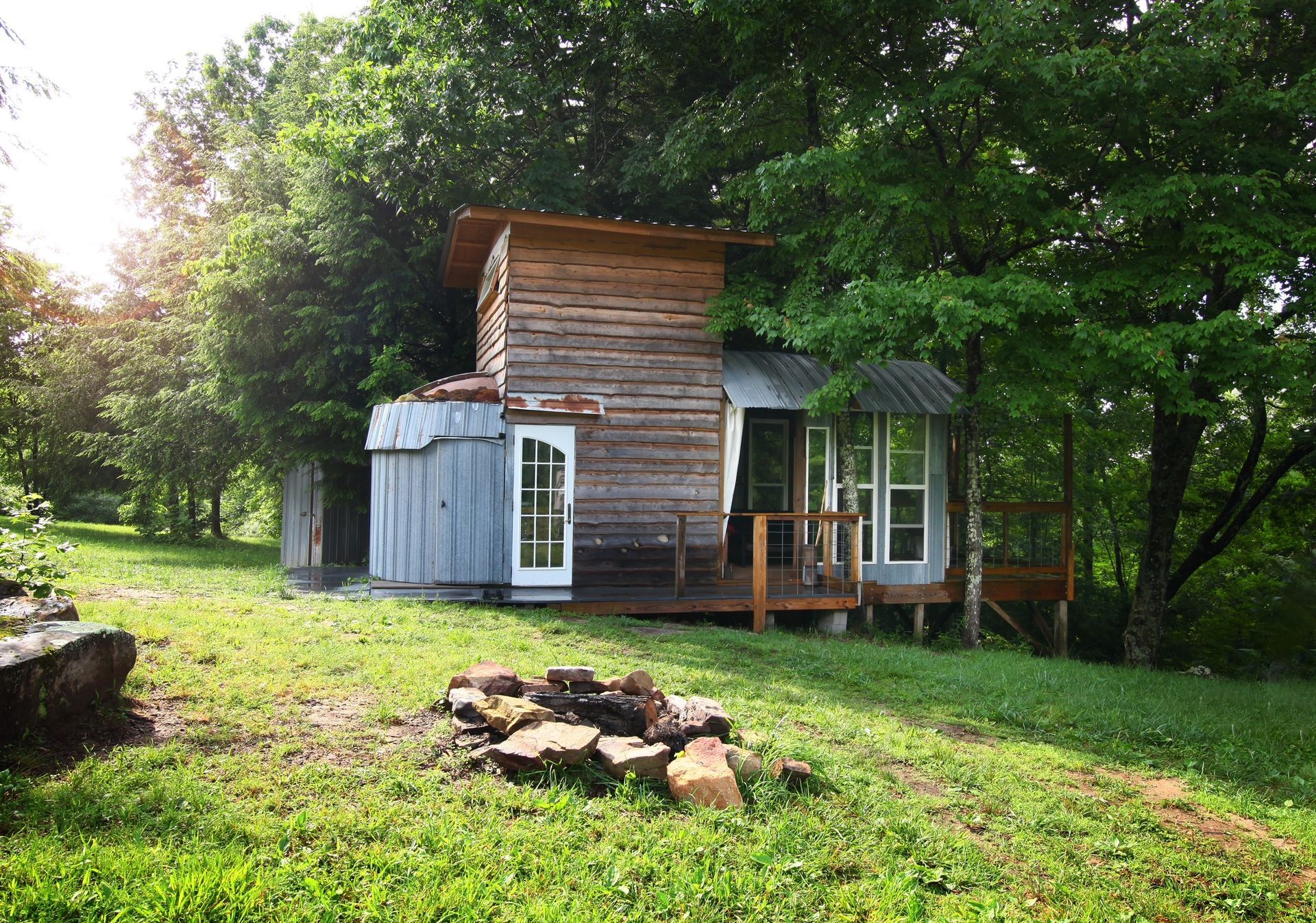 A small wooden house is surrounded by trees and a fire pit.