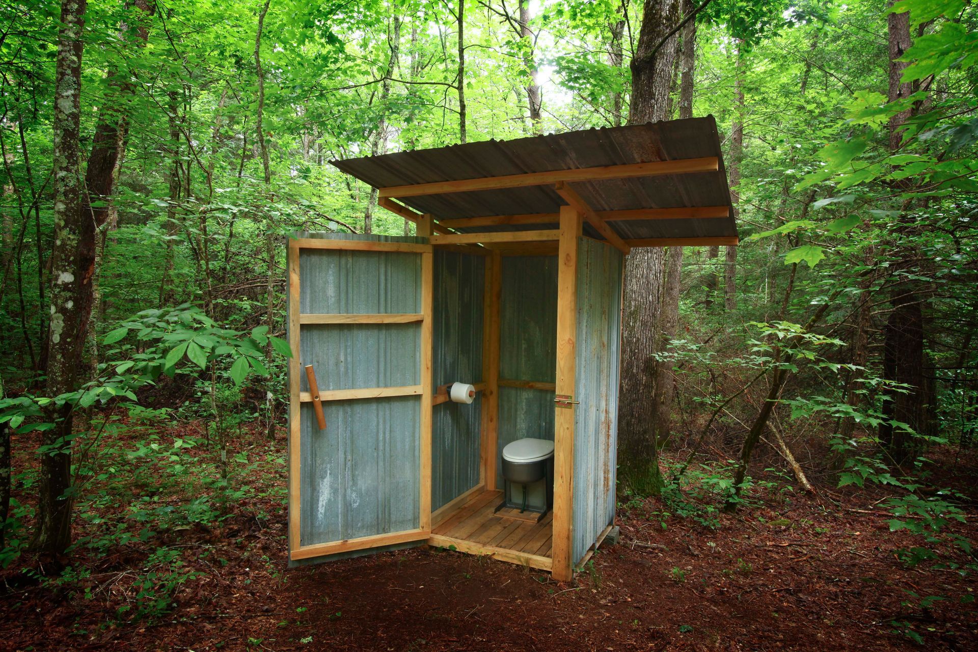 A small outhouse in the middle of a forest with the door open.