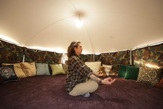 A woman is sitting on the floor in a tent.
