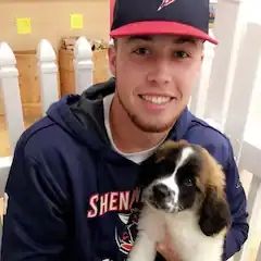 A man in a baseball cap is holding a puppy in his arms.