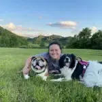 A woman is laying in the grass with two dogs.