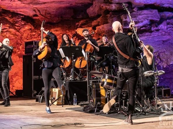 A group of people are playing instruments on a stage in a cave.