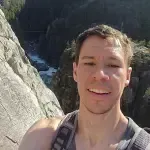 A man is smiling for the camera while standing on top of a mountain.