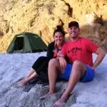 A man and a woman are sitting on the beach in front of a tent.