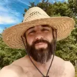 A shirtless man with a beard is wearing a straw hat and necklace.