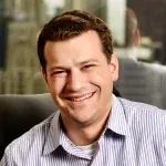 A man in a striped shirt is smiling while sitting in a chair.