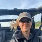 A woman is sitting in the back seat of a car wearing sunglasses and a hat.