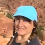 A woman wearing a blue hat and braids is smiling.