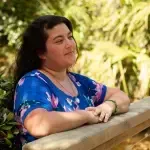 A woman in a blue shirt is leaning on a wooden railing.