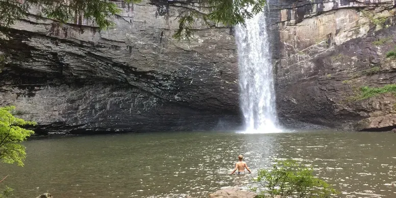 A man is standing in the water near a waterfall.