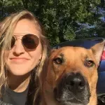 A woman wearing sunglasses is taking a selfie with her dog.