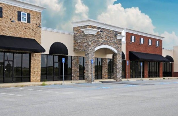 Empty storefronts with awnings, stone and brick exteriors, in a strip mall with blue sky.