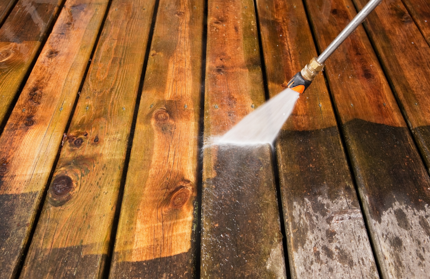 Pressure washing a wooden deck, removing dirt and grime.