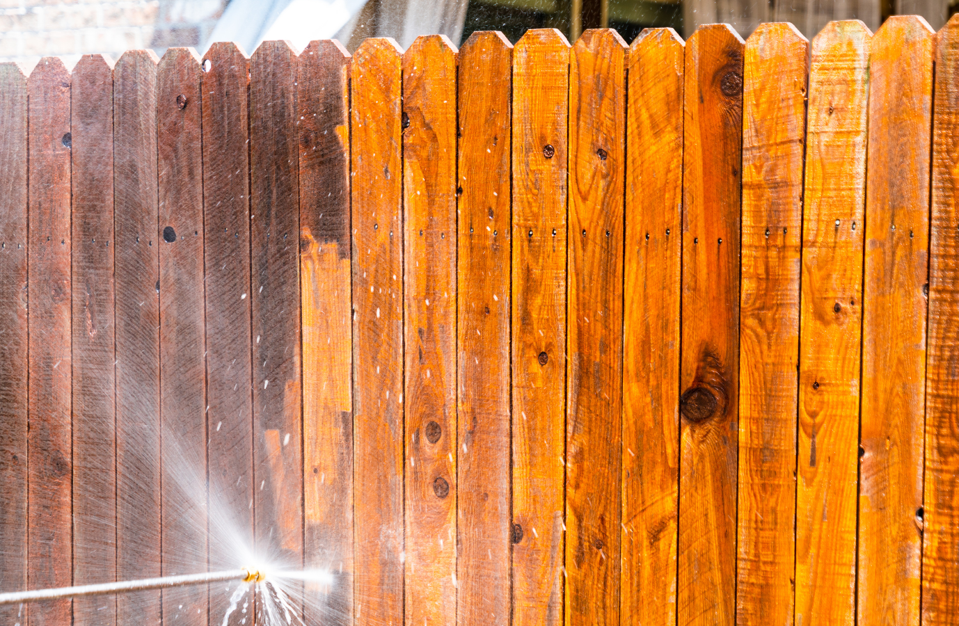 Pressure washing a wooden fence, revealing clean, bright wood.