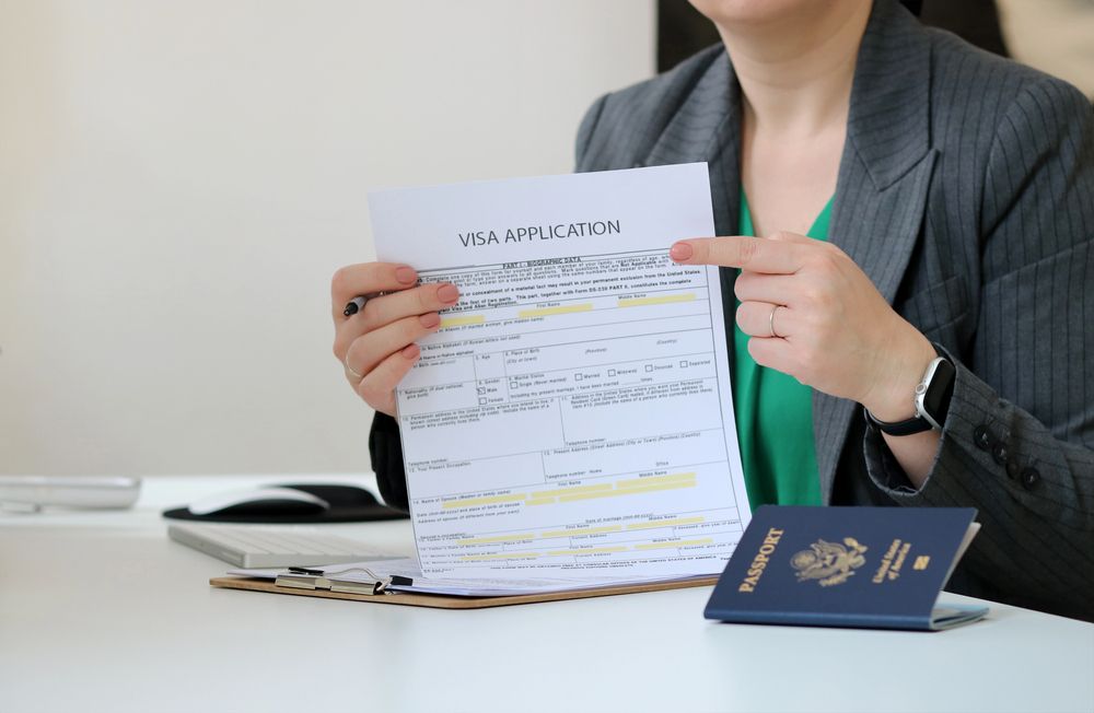 Una persona con chaqueta sostiene un formulario de solicitud de visa y lo señala junto a un pasaporte estadounidense