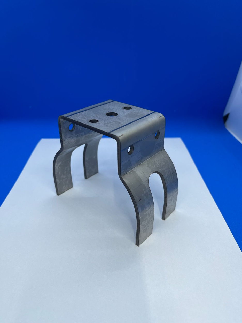 Soporte metálico con patas curvas y placa superior, para montaje, sobre superficie blanca sobre fondo azul.