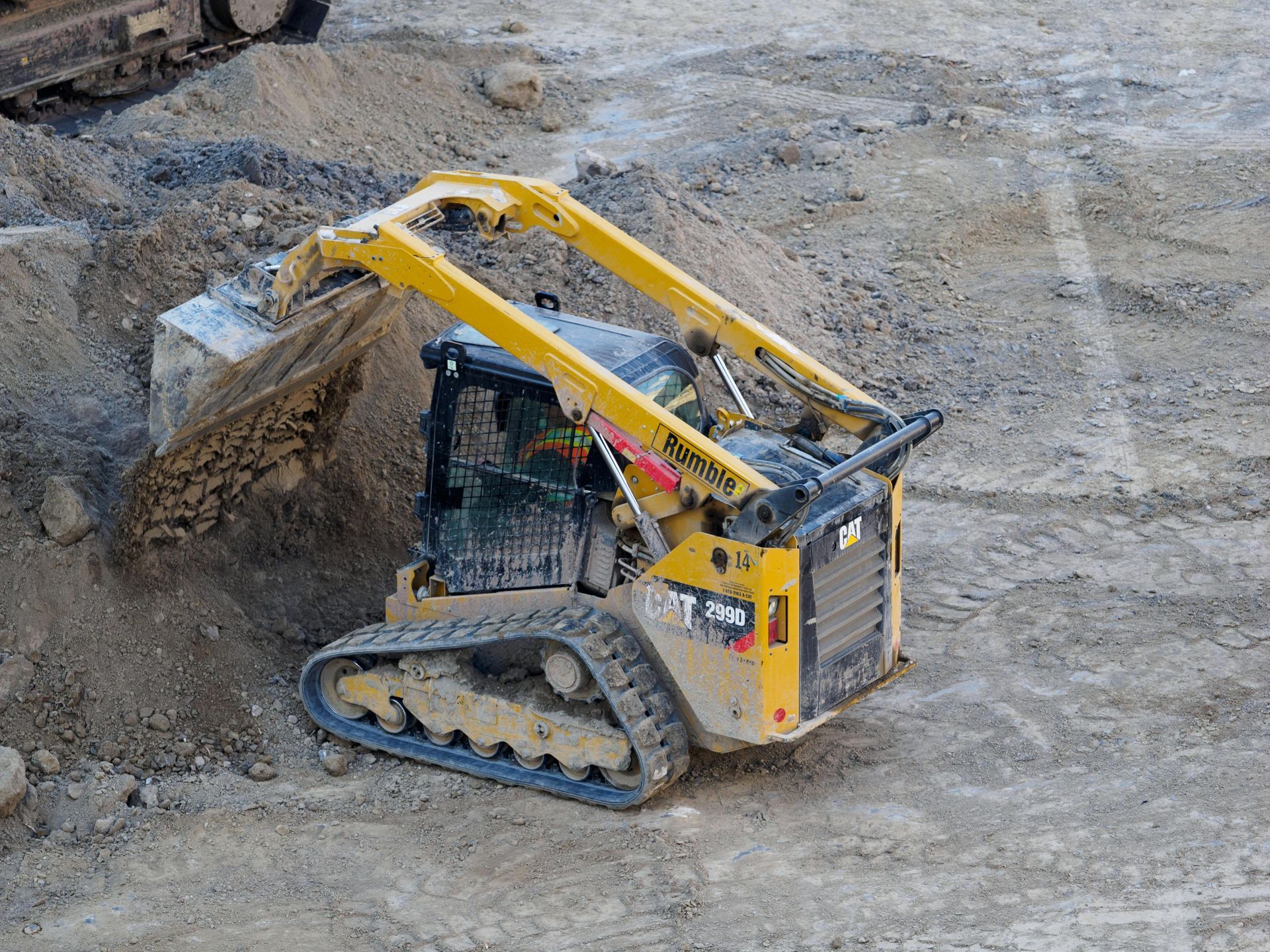 A yellow cat excavator is loading dirt into a dumpster.
