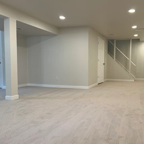 An empty basement with carpeted floors and stairs.