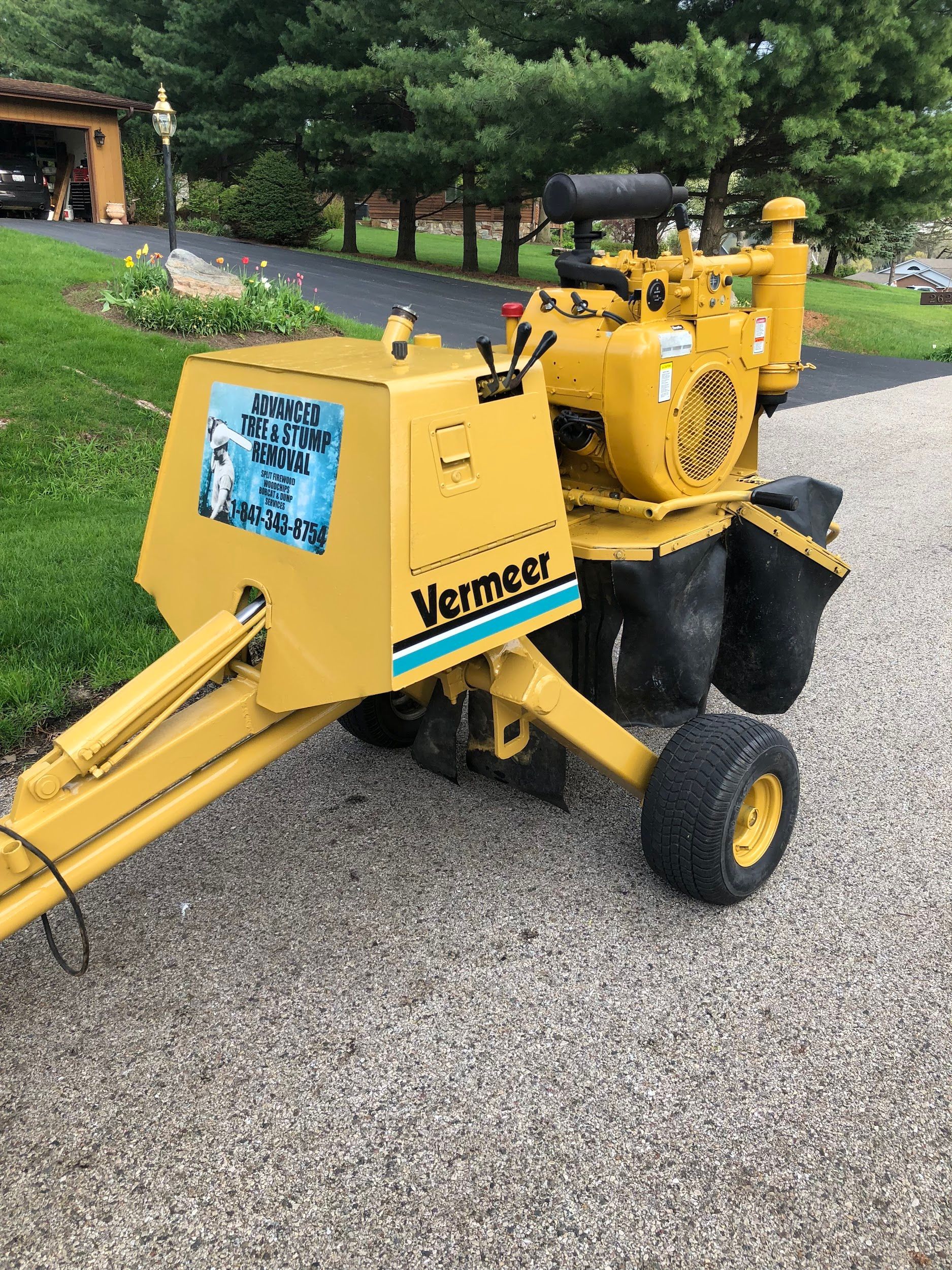 Yellow Vermeer stump grinder on a gravel driveway, ready for use.
