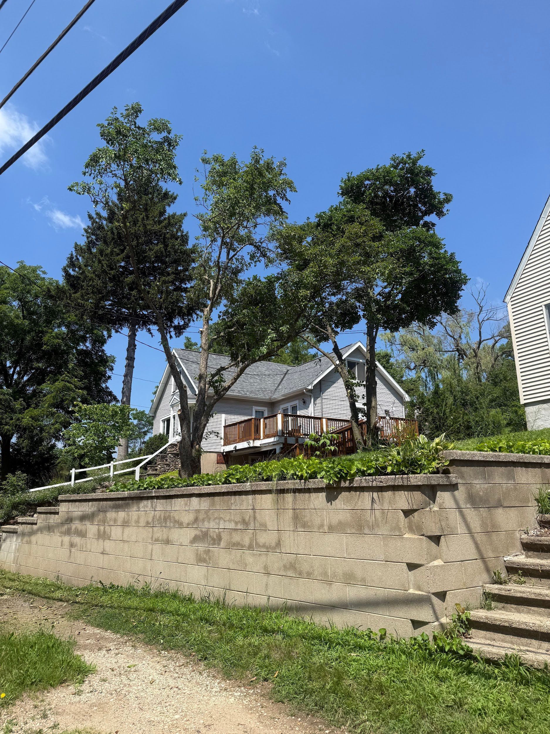 White house with gray roof, trees, and retaining wall against a blue sky.