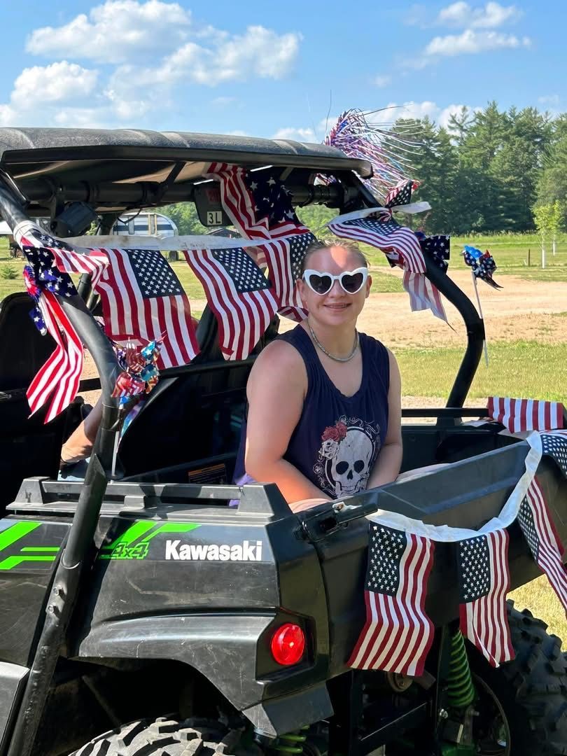 A woman is sitting in a kawasaki atv decorated with american flags.