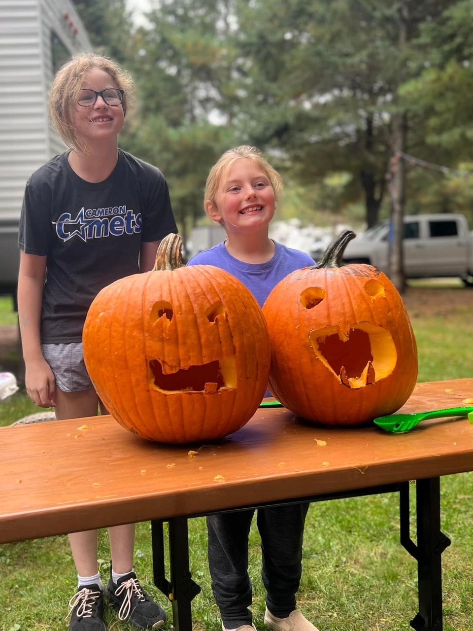 Two young girls are sitting at a table with carved pumpkins.