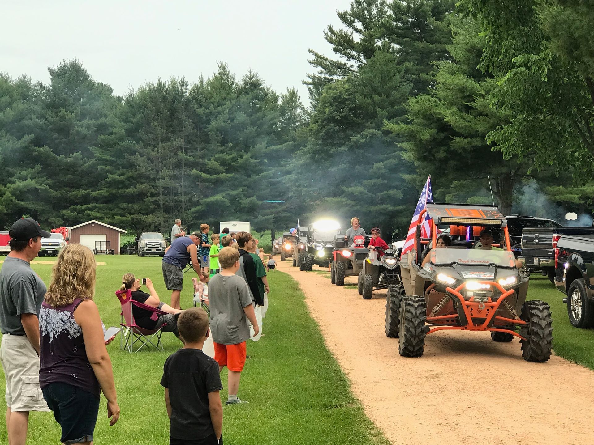 A group of people are watching a parade of atvs driving down a dirt road.