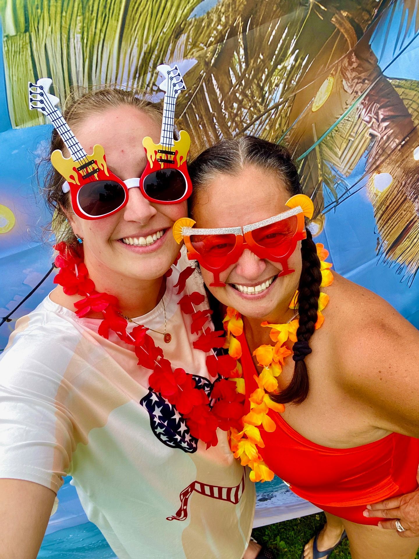 Two women wearing sunglasses and lei are posing for a picture.