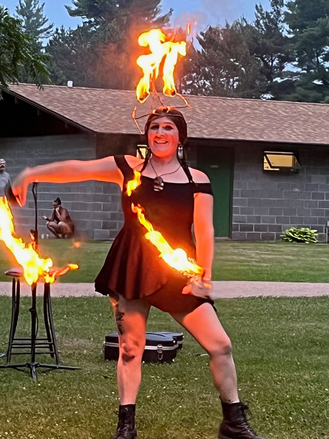A woman in a black dress is holding a torch with flames on it.