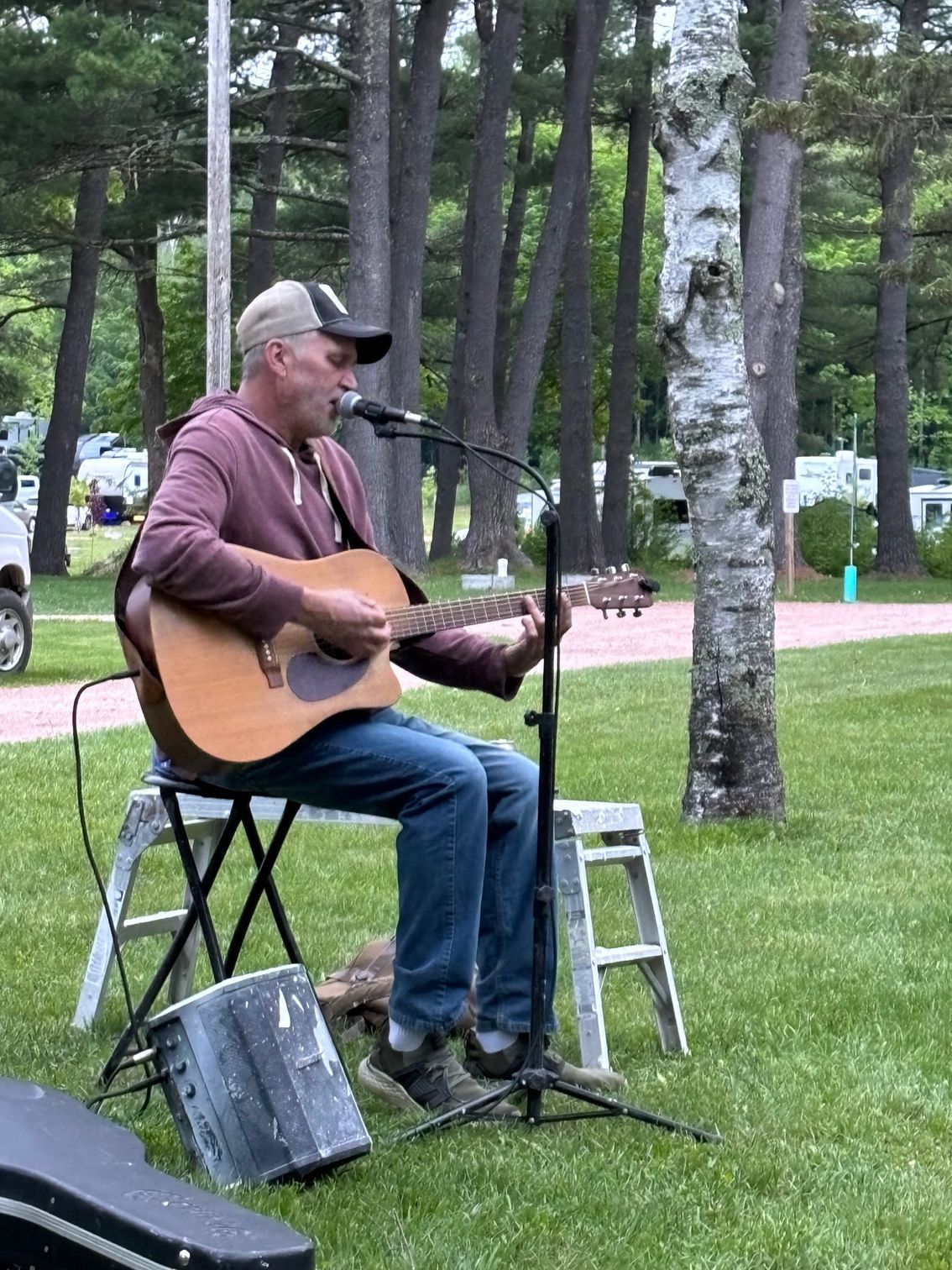 A man is sitting on a stool playing a guitar and singing into a microphone.
