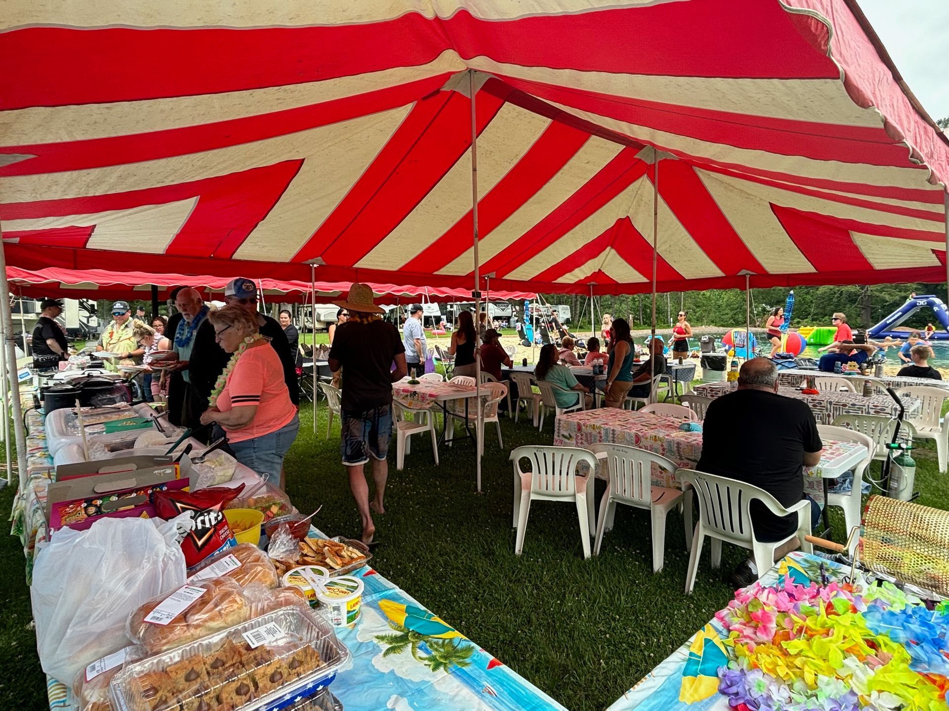 A group of people are sitting at tables under a red and white tent.