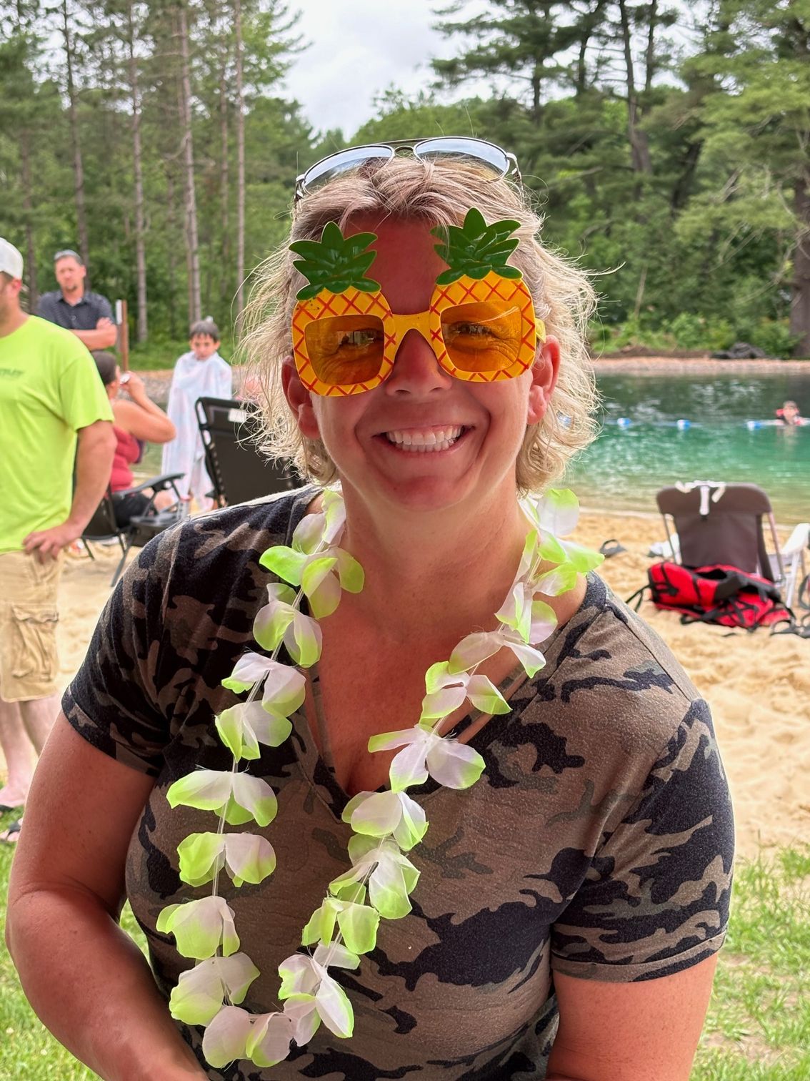 A woman wearing pineapple sunglasses and a lei is smiling.