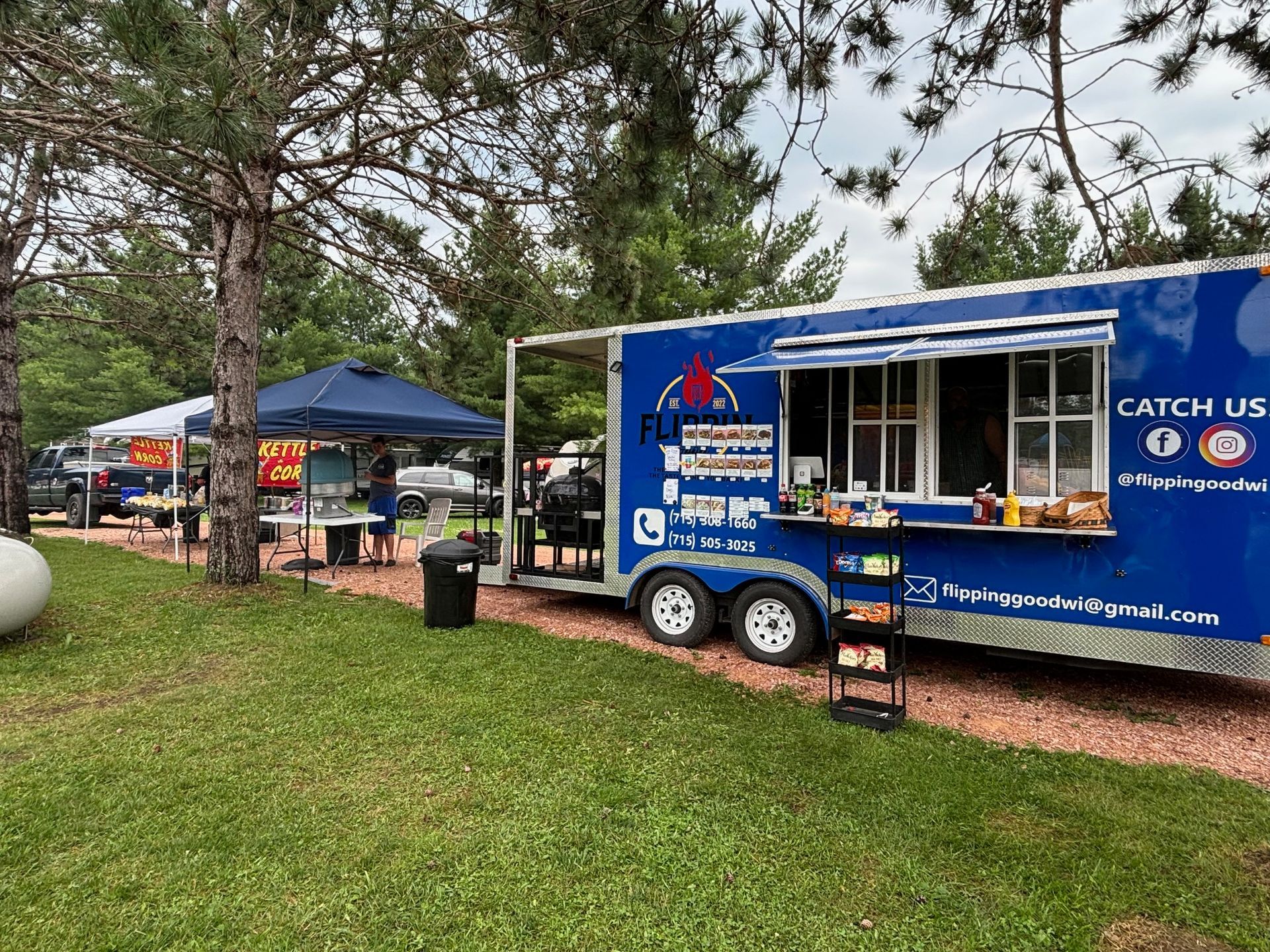 A blue food truck is parked in a grassy field.