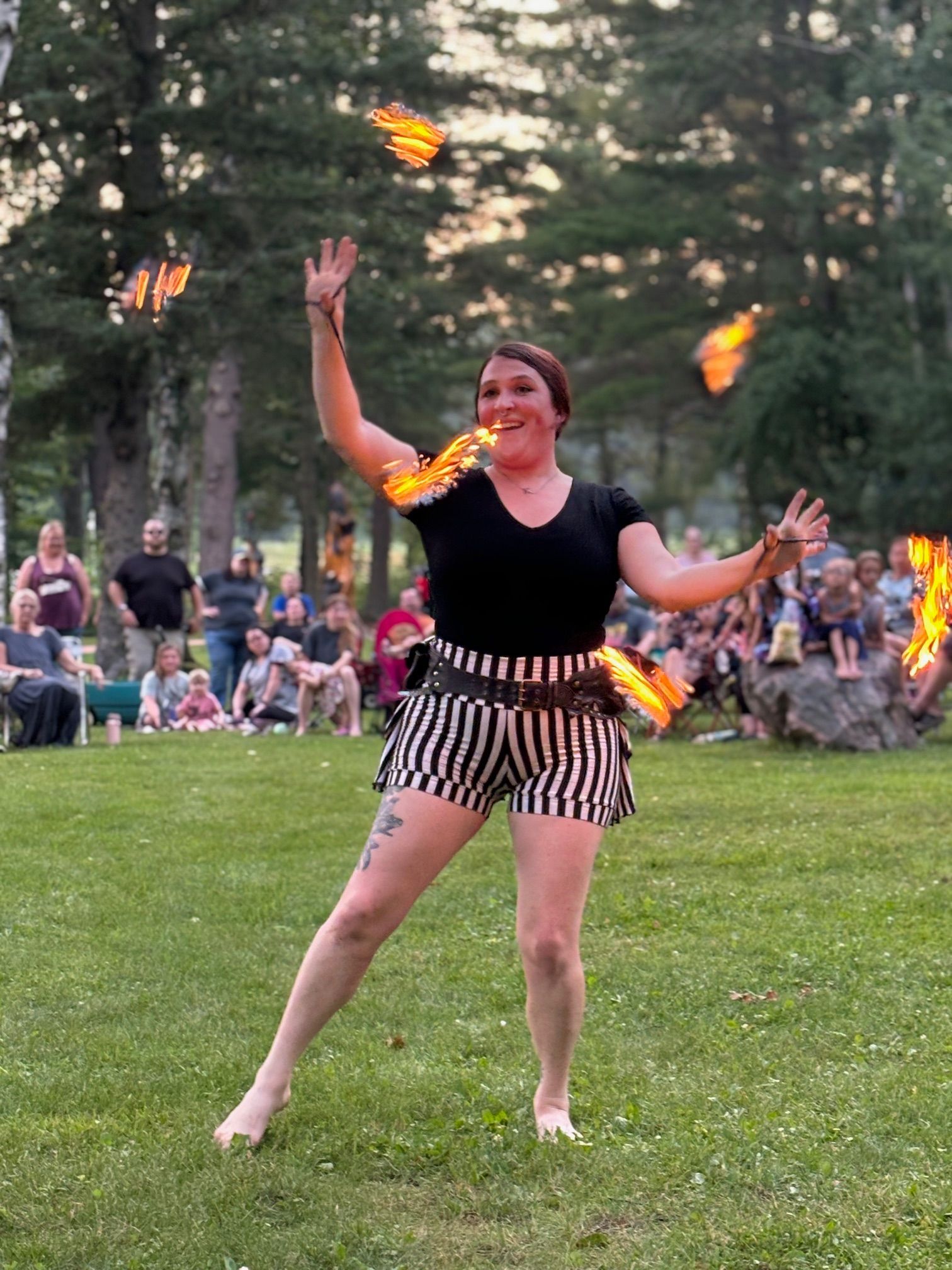 A woman is juggling fire in a park in front of a crowd.