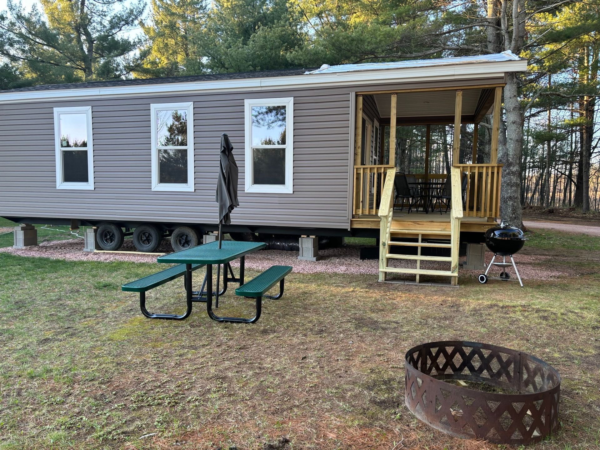 A mobile home with a picnic table and a fire pit in front of it.