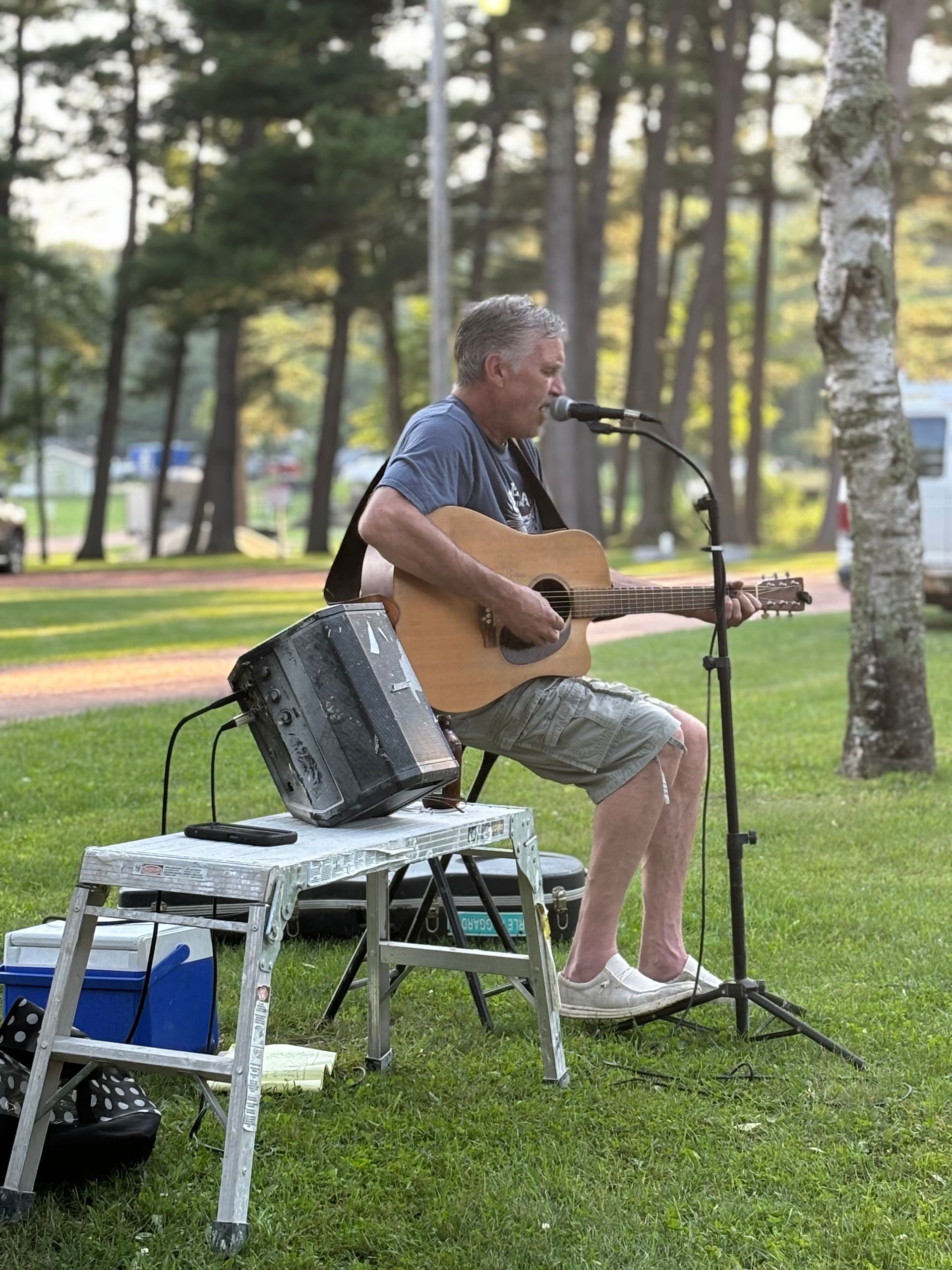 A man is sitting on a stool playing a guitar and singing into a microphone.